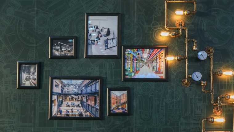 Exhibition of photographs of modern interiors against a dark green wall with steampunk lighting apparatus